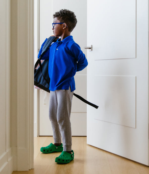 Boy putting on backpack in doorway